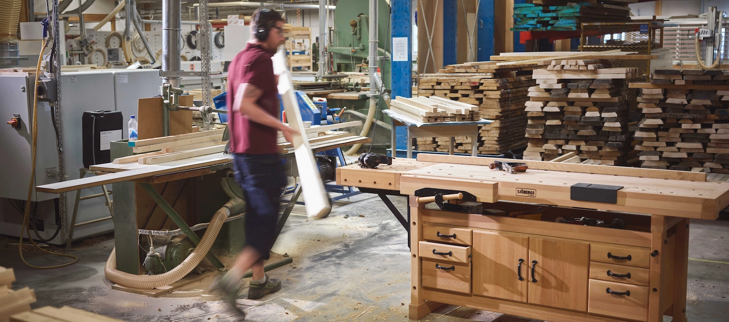 En kille i en verkstad bär på en träplanka